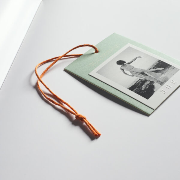 Product label with an orange string on a light background. The label features a black and white photo of a person and a minimalist design.