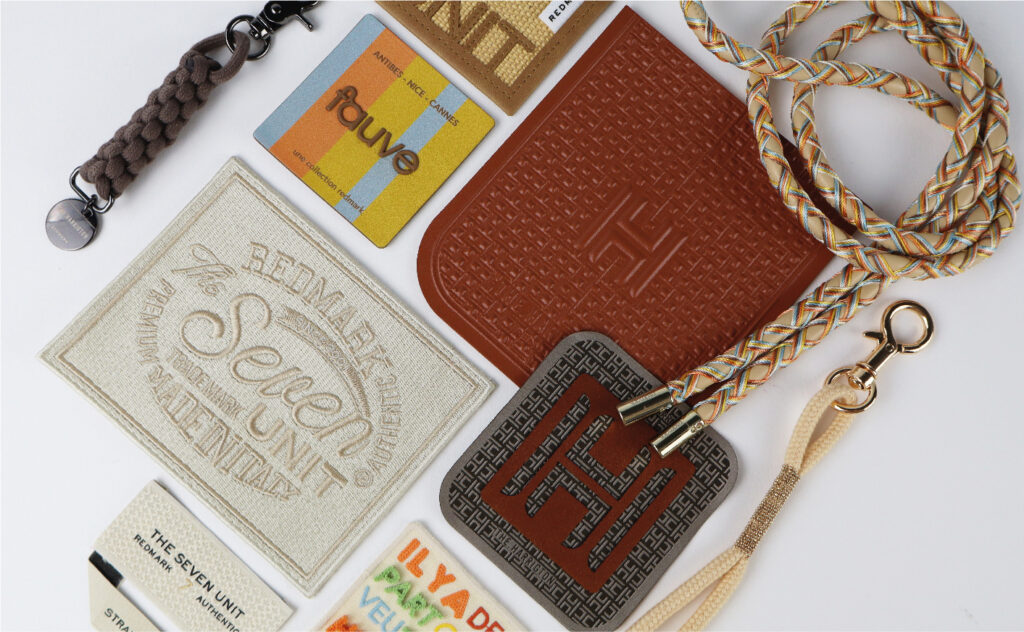 Assorted branding and packaging elements including embroidered patches, woven cords, tags, and textured labels from various collections like Redmark, The Seven Unit, and fauve, displayed on a white background